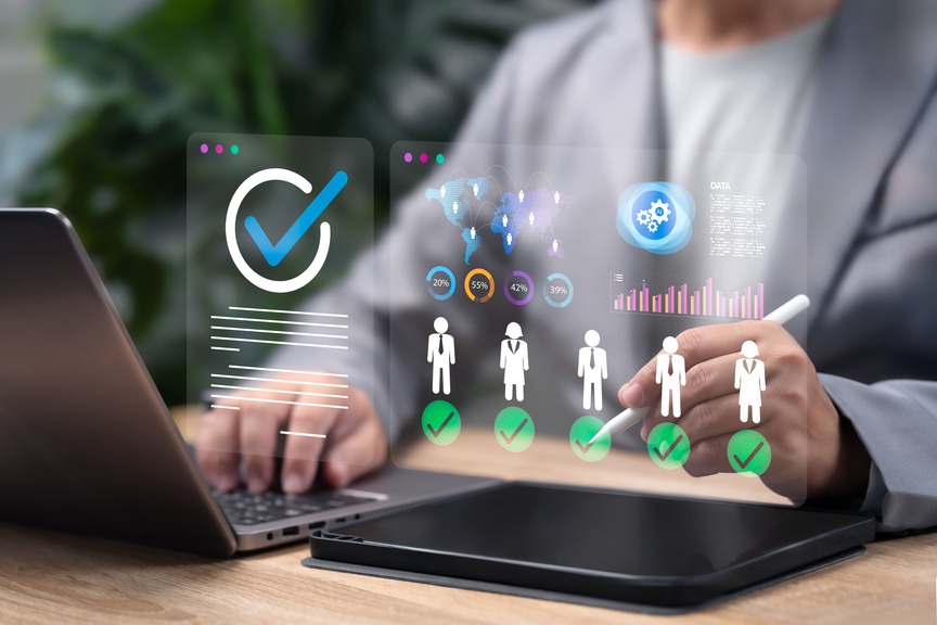 Person using a laptop and tablet while reviewing candidate profiles with charts, percentages, and approval checkmarks on a digital interface.